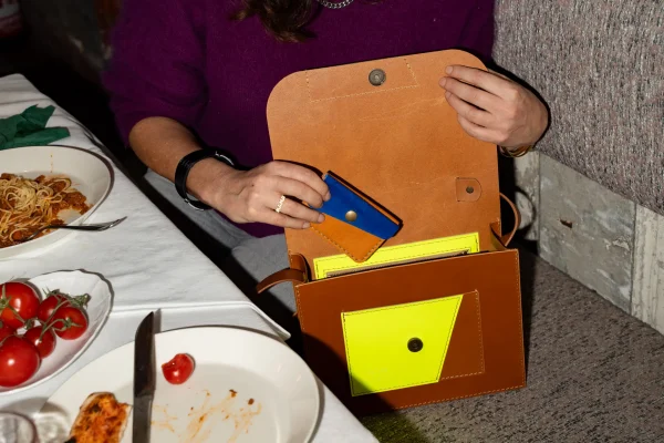 Vrouw steekt een cognac Halle B. portefeuille met kobaltblauw in een cognac Sofie L. handtas met fluogeel.