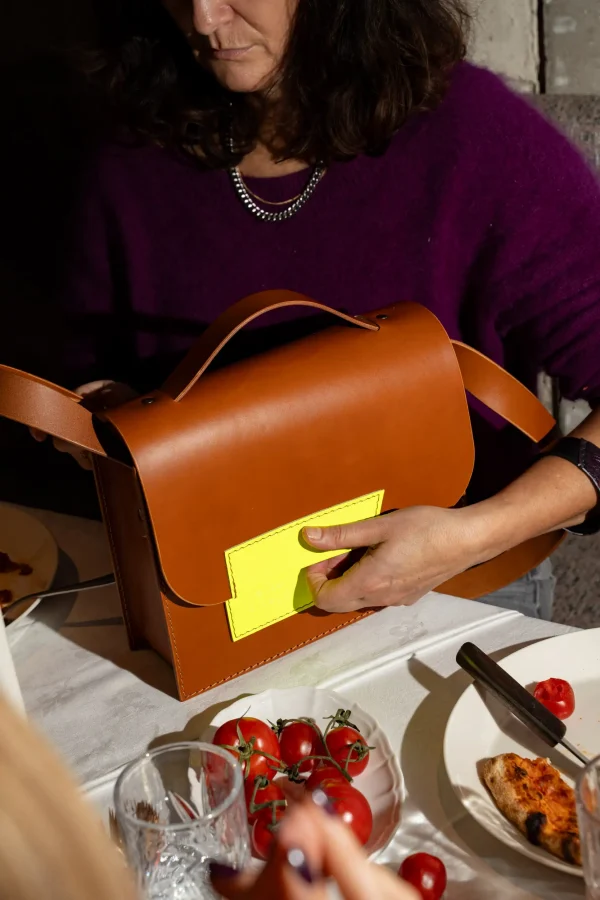 Vrouw opent de cognac Sofie L. handtas met fluogeel contrast.