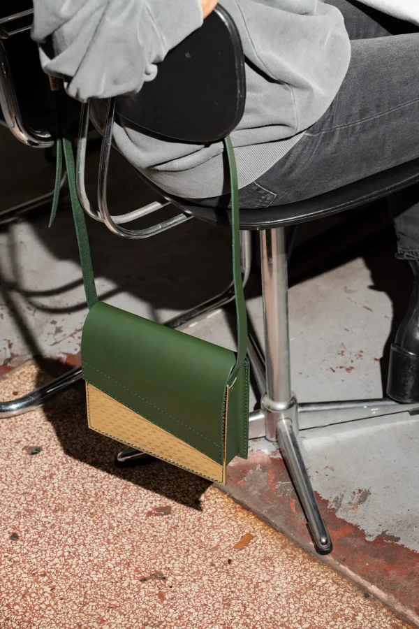 De groene Reese W. handtas met gouden front hangt aan een stoel.