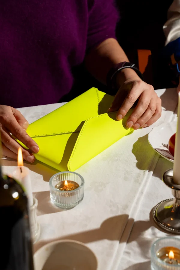 Vrouw heeft de fluogele Billie E. enveloppetas in de hand en draagt The Double Bold armband in zwart en paars.