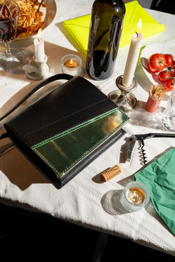 De zwarte Reese W. handtas met groen métallic front en een fluogele Billie E. enveloppetas liggen op tafel.