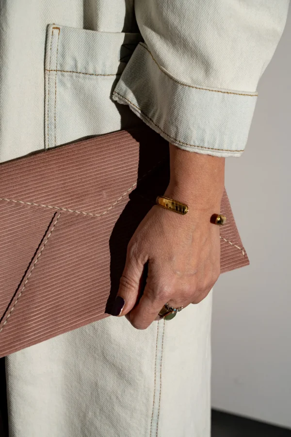 Vrouw heeft vuilroze gestreepte Billie E. enveloppetas in de hand.