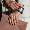 Vrouw heeft vuilroze gestreepte Billie E. enveloppetas in de hand en pruts ondertussen aan haar kobaltblauwe The Bold armband met rosé métallic contrast.