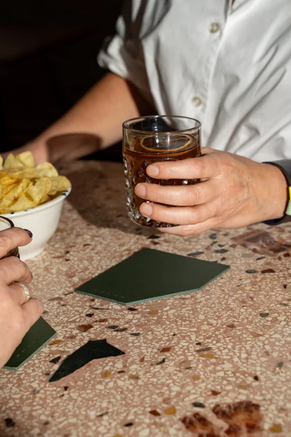 Twee vrouwen heffen het glas die op groene coasters staan.