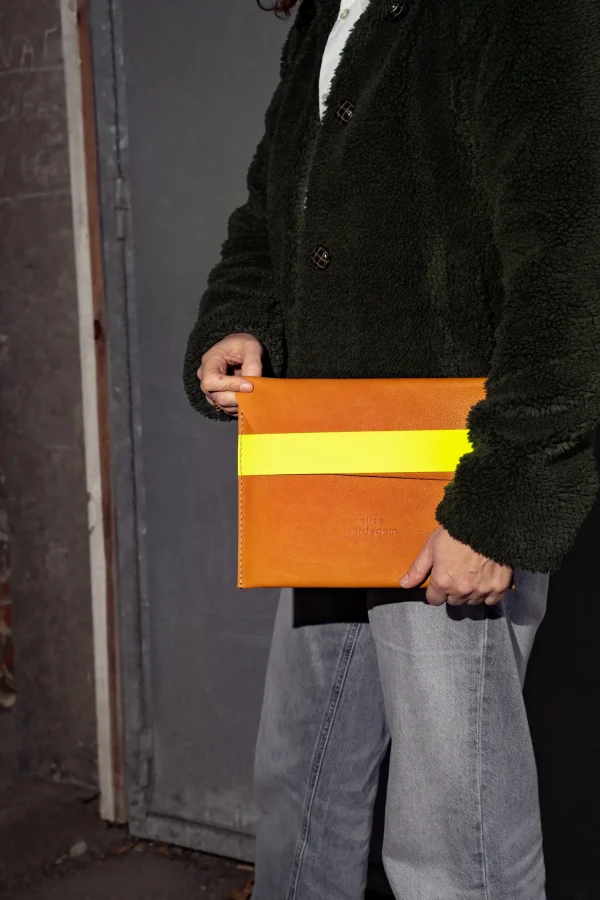 Model draagt de cognac tabletsleeve Kate W. met fluogele riem onder de arm.