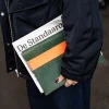 Petrolkleurige tabletsleeve Kate W. met oranje sluitriem onder de arm van een model.