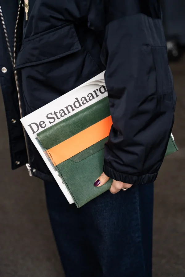 Petrolkleurige tabletsleeve Kate W. met oranje sluitriem onder de arm van een model.